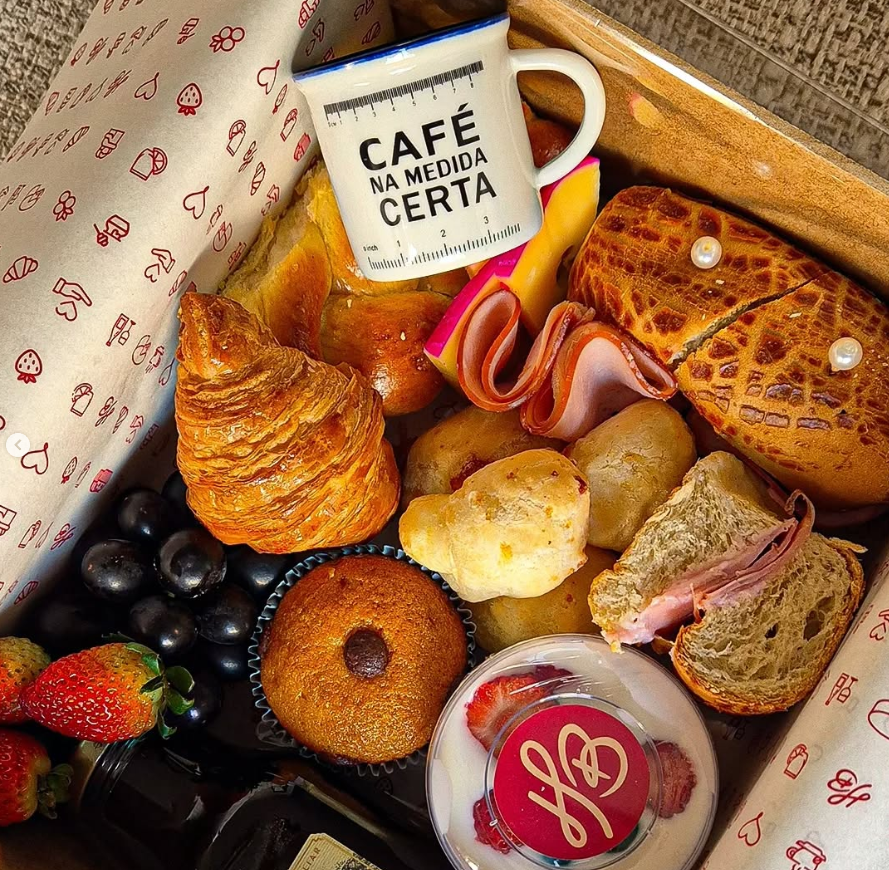 Cesta de café da manhã com pães, frutas e suco.